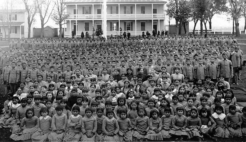 A group photo of Native American children outside of a tribal boarding school.