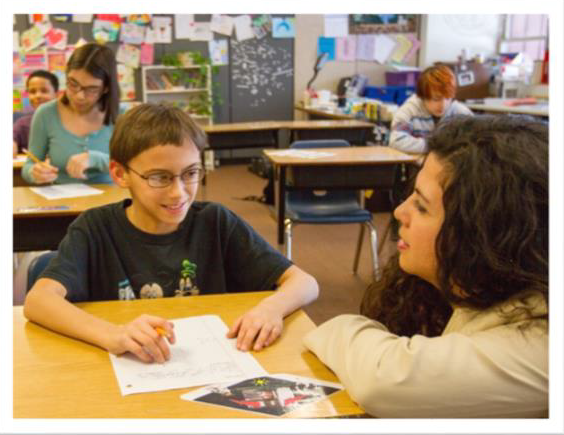 A teacher talking to a student at his desk.