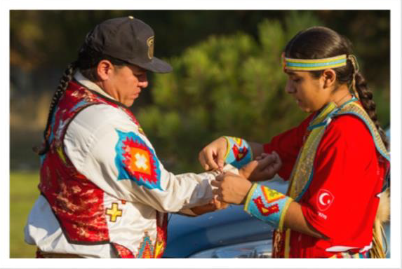 A Native American male teenager helping button up a shirt sleeve for his father.