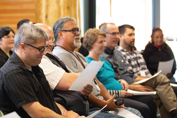 A group of five individuals seated in a row, each holding papers and engaged in discussion.